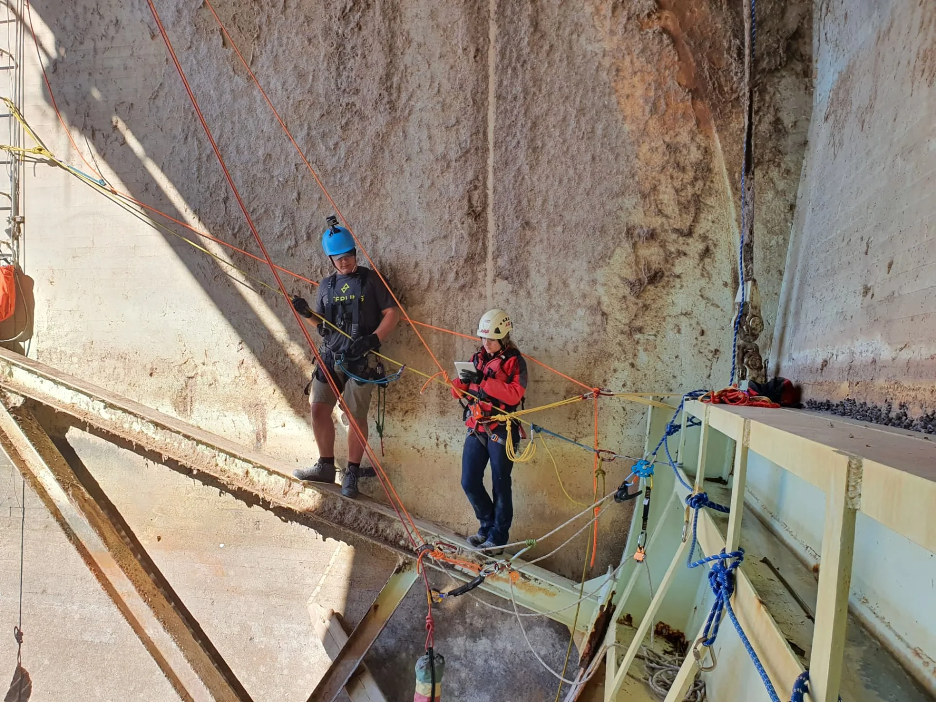 Two harnessed workers managing ropes and equipment inside a concrete industrial structure