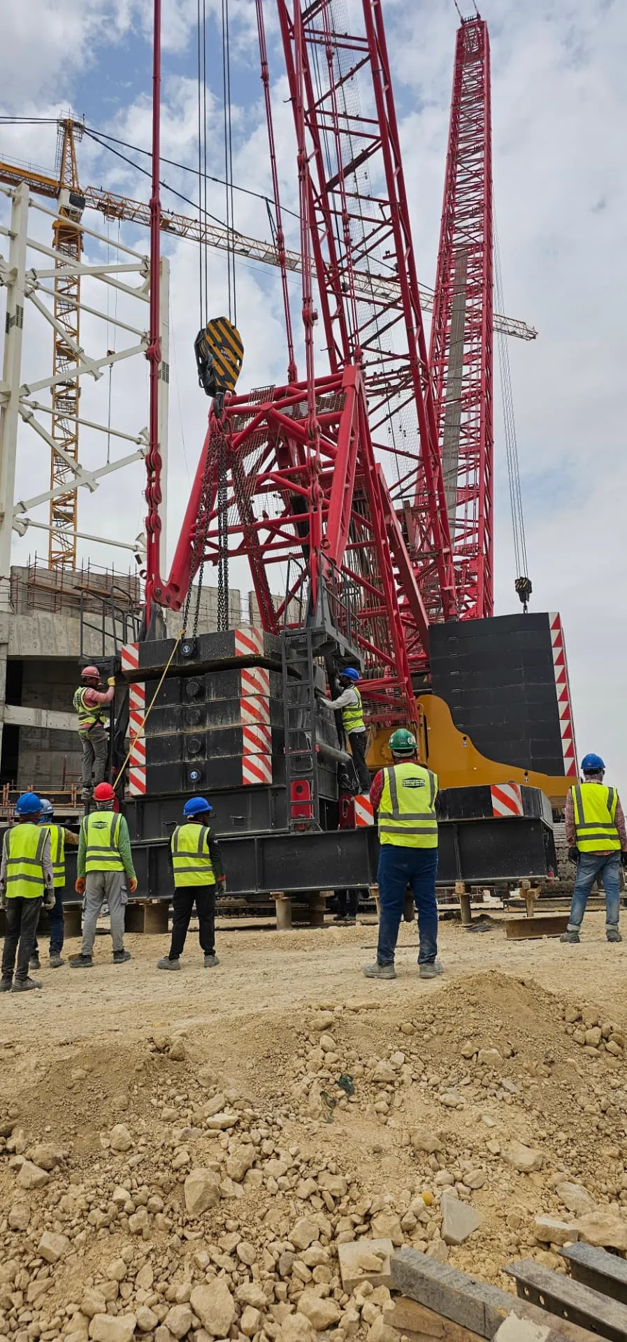 Crew in high-visibility PPE observing counterweight installation during crawler crane assembly